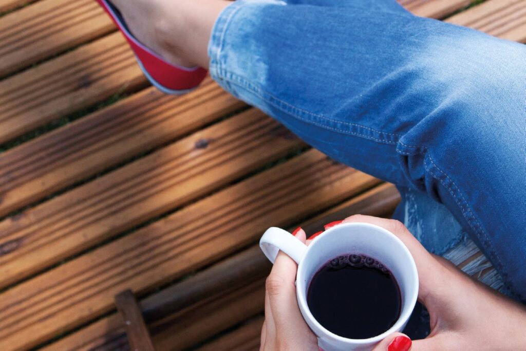 Gepflegte Holzterrasse Person mit Kaffeetasse auf einer gepflegten Holzterrasse
